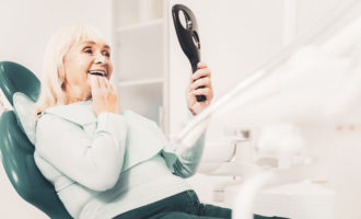 Old woman in dentist's chair looking at her new teeth